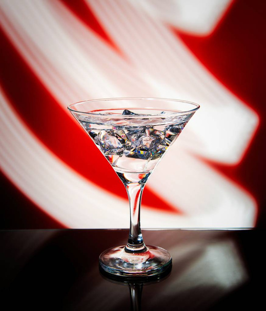 Vidrio Martini aislado sobre un fondo rojo con rayas de pintura de luz de neón detrás de ellos. Onda de luz, juego de colores, dibujo con luz
. - Foto, imagen