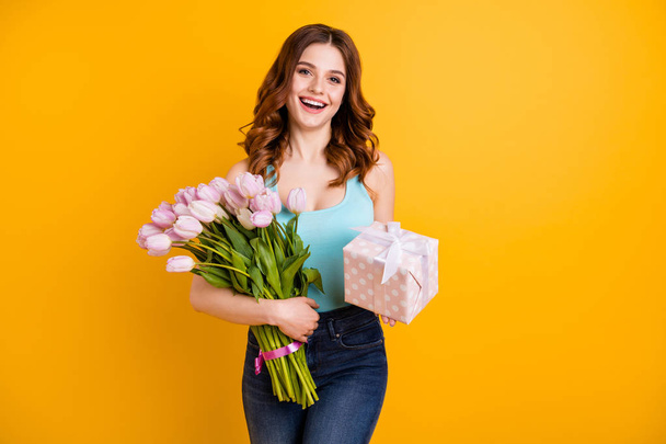 Portrait of pretty lady holding big bunch of pink tulips in arms and giftbox wear tank-top and jeans isolated yellow background - Fotografie, Obrázek