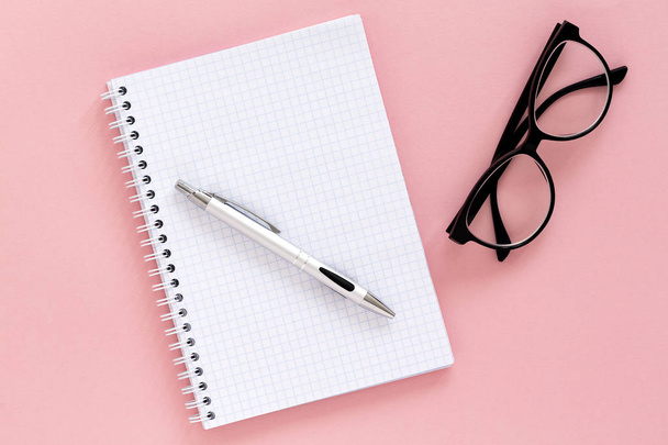 Notebook, pen and glasses on pink background. Spiral notepad on a table. Top view with copy space. - Foto, imagen