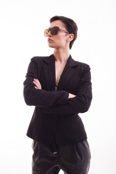Attractive fashion model posing in black jacket wearing sunglasses over white background in studio - Foto, Imagen