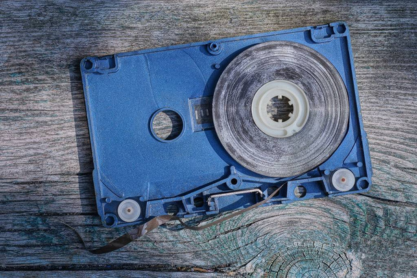 een oude blauwe gedemonteerde cassette met een bruine audio tape ligt op een grijze tafel - Foto, afbeelding
