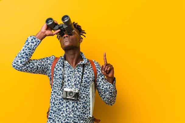 Jeune touriste africain debout sur un fond jaune tenant une jumelle
 - Photo, image