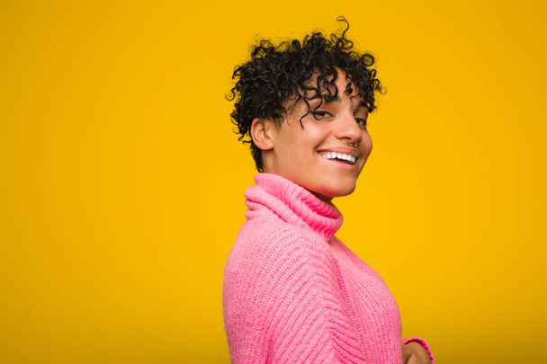 Молодий афроамериканець жінка одягнений у рожевий светр дивиться в сторону посміхаючись, веселий і приємний. - Фото, зображення