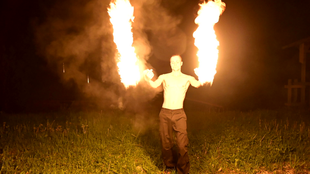 Slow motion of a young man in black pants in total darkness shows a representation of a rotating burning torch. Meditation in motion. Calm and unwavering. Work with fire. Low key - Footage, Video