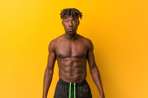 Young black man shirtless wearing swimsuit blows cheeks, has tired expression. Facial expression concept. - Fotografie, Obrázek