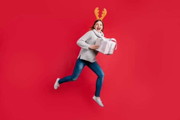 Funky lady holding big giftbox Santa consegna usura copricapo corna e pullover a maglia isolato sfondo rosso
 - Foto, immagini