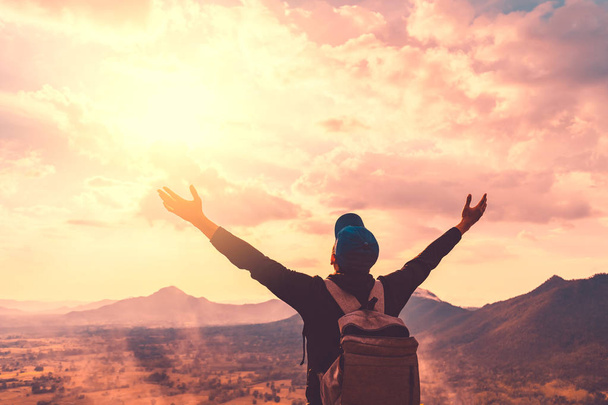 Backpacker άνθρωπος Σηκώστε το χέρι επάνω στην κορυφή του βουνού με το ηλιοβασίλεμα του ουρανού και σύννεφα αφηρημένα φόντο. - Φωτογραφία, εικόνα