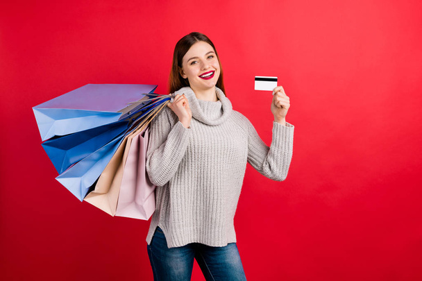 Pretty lady holding many packs and plastic card in hands wear knitted sweater isolated red background - 写真・画像