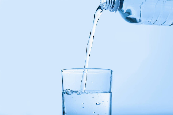 Pouring water from bottle into glass against blue background. Refreshing drink - Foto, afbeelding