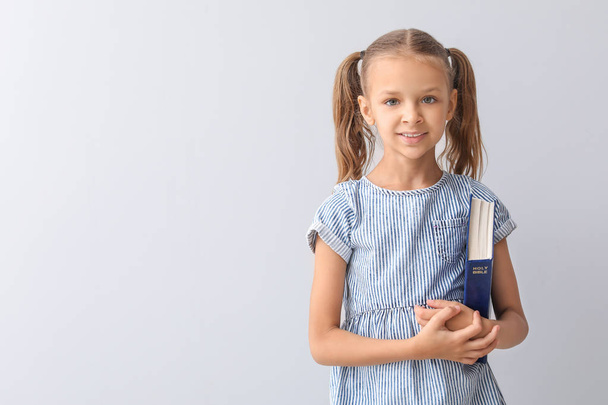 Cute little girl with Bible on light background - Photo, Image