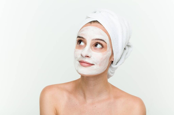 Young caucasian woman enjoying of a facial mask treatment - 写真・画像