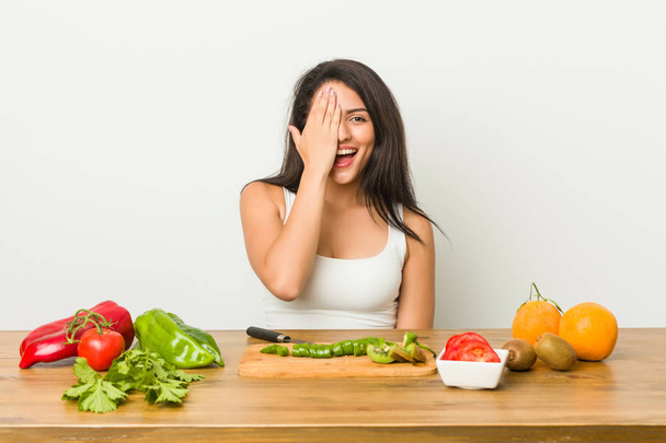 Young curvy woman preparing a healthy meal having fun covering half of face with palm. - Foto, Imagem