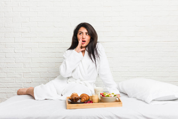 Młoda krzywego kobieta biorąc śniadanie na łóżku mówi tajne wiadomości na gorąco hamowania i patrząc na bok - Zdjęcie, obraz