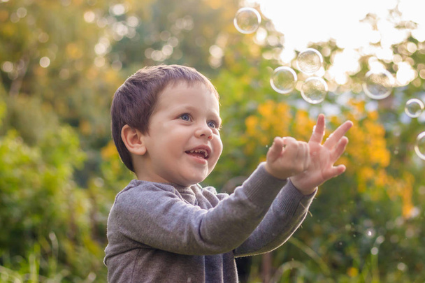 A boy on the street catches soap bubbles. Happy childhood. Childrens games. - Photo, Image