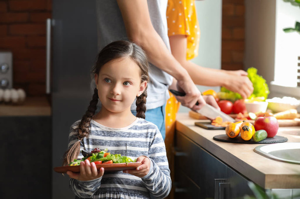 Petite fille avec des parents préparant une salade de légumes dans la cuisine
 - Photo, image