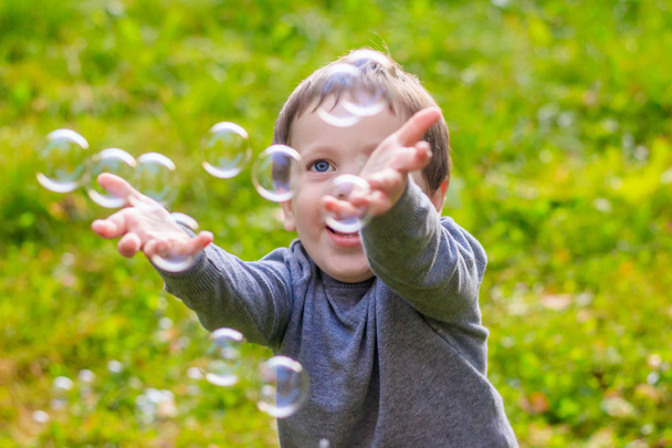 Een jongen op straat vangt zeepbellen. Gelukkige kindertijd. Kinderspelletjes. - Foto, afbeelding