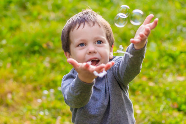 Een jongen op straat vangt zeepbellen. Gelukkige kindertijd. Kinderspelletjes. - Foto, afbeelding