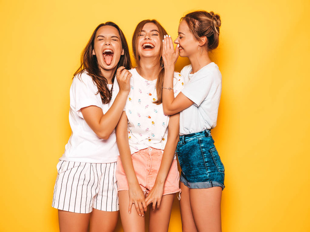 Three young beautiful smiling hipster girls in trendy summer clothes. Sexy carefree women posing near yellow wall in studio. Positive models going crazy and having fun.Hugging - Foto, immagini