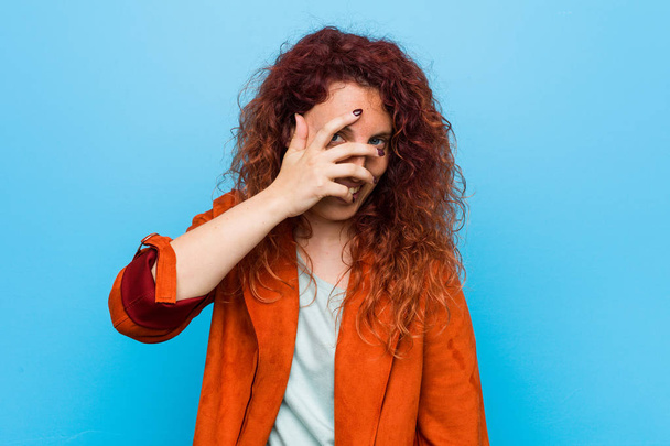 Young redhead elegant woman blink at the camera through fingers, embarrassed covering face. - Foto, Bild