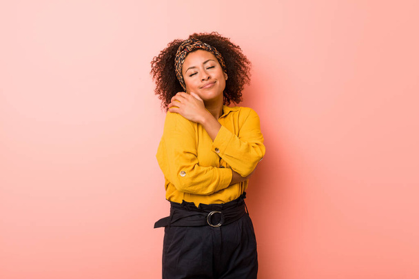 Joven mujer afroamericana sobre un fondo rosado abrazos, sonriente despreocupado y feliz
. - Foto, Imagen