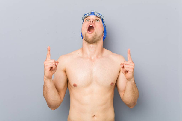 Young professional swimmer man pointing upside with opened mouth. - Photo, Image