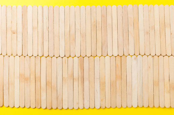 Muchos palitos de helado de madera en fila sobre fondo amarillo, plana l
 - Foto, imagen