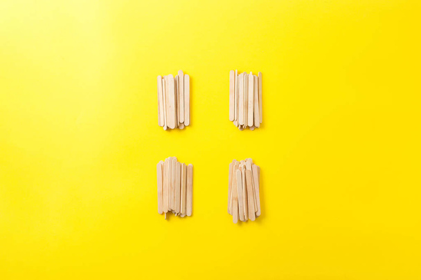 Несколько кучи деревянных палочек мороженого на желтом фоне. C
 - Фото, изображение