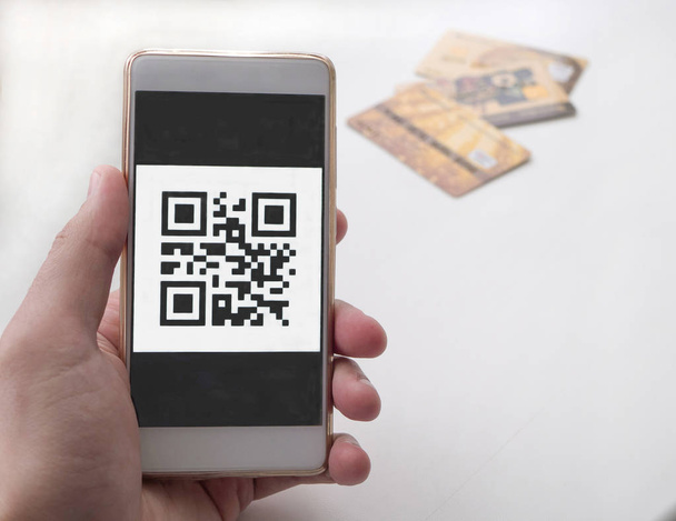 Ręka trzyma inteligentny telefon z kodem QR. 3 karty bankowe na oświetlenie tła - Zdjęcie, obraz