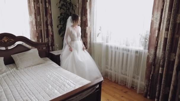 Krásná a krásná nevěsta na svatebních šatech u okna. Krásná žena - Záběry, video