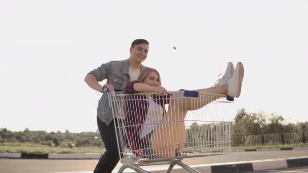 Young friends having fun on shopping trolleys. Multiethnic young people racing on shopping cart. slow motion. - Materiaali, video