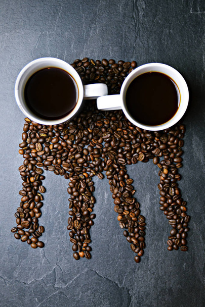 Koffiebonen op een zwarte achtergrond vormen het silhouet van een kwal en twee kopjes koffie vormen hun ogen - concept met koffie en kwallen - Foto, afbeelding