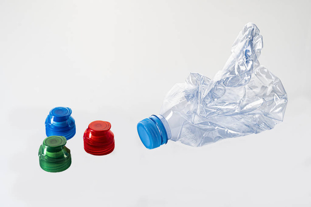 Frasco de plástico usado con tapón azul para reciclar con tres tapones aislados de color rojo, verde y azul sobre un fondo blanco. Contaminación ambiental
 - Foto, imagen