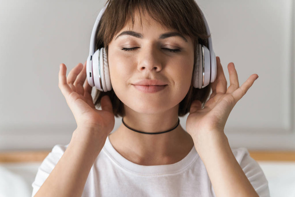 Relaxing young beautiful woman indoors at home listening music with headphones. - Foto, imagen