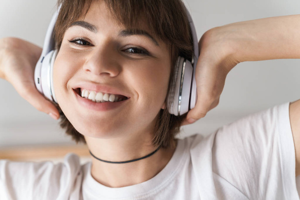 Smiling young beautiful woman indoors at home listening music with headphones. - Fotoğraf, Görsel