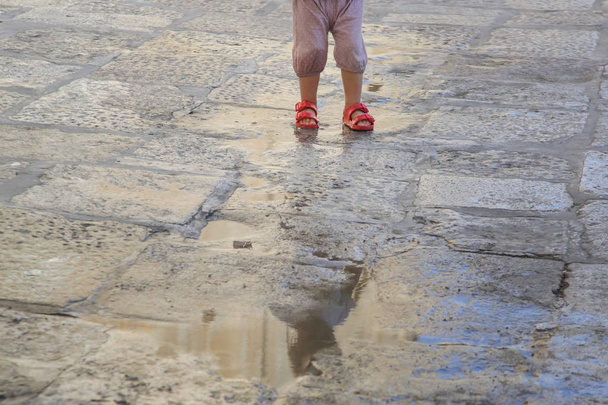 Pies de niño en sandalias de goma roja saltando en un charco de lluvia
 - Foto, imagen