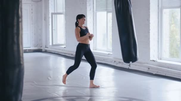 Kickboxing athlète professionnelle femme donne un coup de pied dans le sac de coups de poing dans la salle de gym. Taekwondo athlétique femme s'entraînant dans la salle de gym
. - Séquence, vidéo