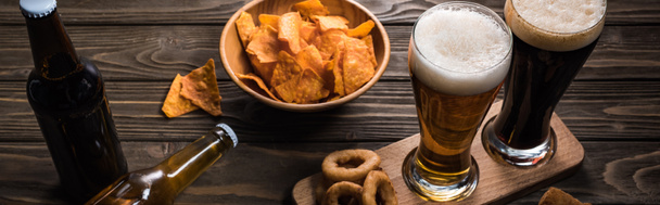 панорамний знімок келихів легкого і гарячого пива біля пляшок і закусок на дерев'яному столі
 - Фото, зображення