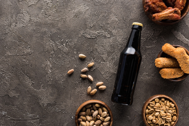 vista dall'alto di bottiglia di birra scura vicino a ciotole con noci e spuntini di pollo sulla superficie marrone
 - Foto, immagini