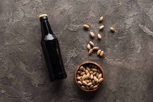 top view of bowl with pistachios near bottle of dark beer on brown surface - Foto, Bild
