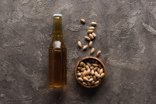 top view of bowl with pistachios near bottle of light beer on brown surface - Foto, Imagem