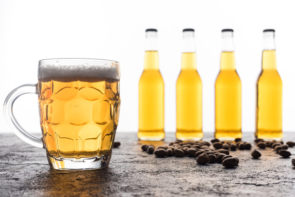 Bögre világos sör közelében palackok és kávésszemek a barna textúrájú felületen - Fotó, kép