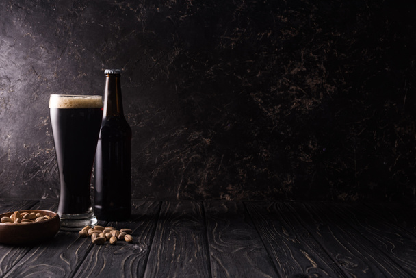 bottiglia e bicchiere di birra vicino ciotola con pistacchi sul tavolo di legno
 - Foto, immagini