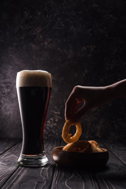 przycięte widok człowieka biorąc smażony pierścień cebuli w pobliżu szklanki piwa na drewnianym stole - Zdjęcie, obraz