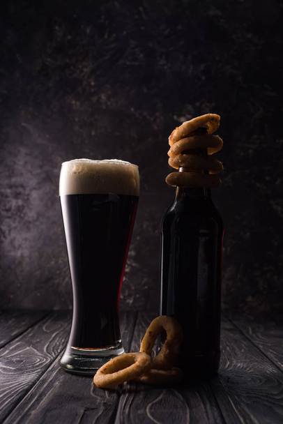 стекло и бутылка пива с жареными луковыми кольцами на деревянном столе
 - Фото, изображение