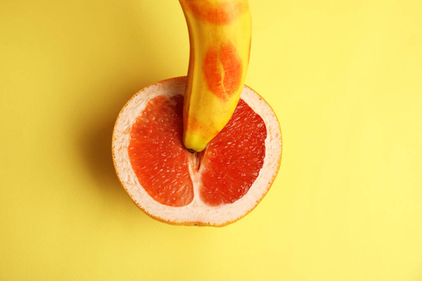 Fresh grapefruit and banana with red lipstick marks on yellow background, flat lay. Sex concept - Foto, Imagen