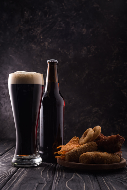 láhev a sklenice piva blízko talíře s občerstvením na dřevěném stole - Fotografie, Obrázek