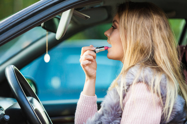 Young woman applying lipstick in car - Foto, afbeelding