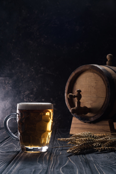 caneca de cerveja leve perto de pequeno barril e picos de trigo na mesa de madeira
 - Foto, Imagem