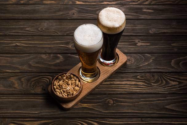 vasos de cerveza oscura y ligera cerca de cuenco con cacahuetes asados en mesa de madera
 - Foto, Imagen
