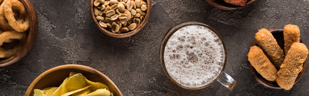 plano panorámico de taza de cerveza ligera cerca de cacahuetes y patatas fritas en la superficie de textura marrón
 - Foto, Imagen
